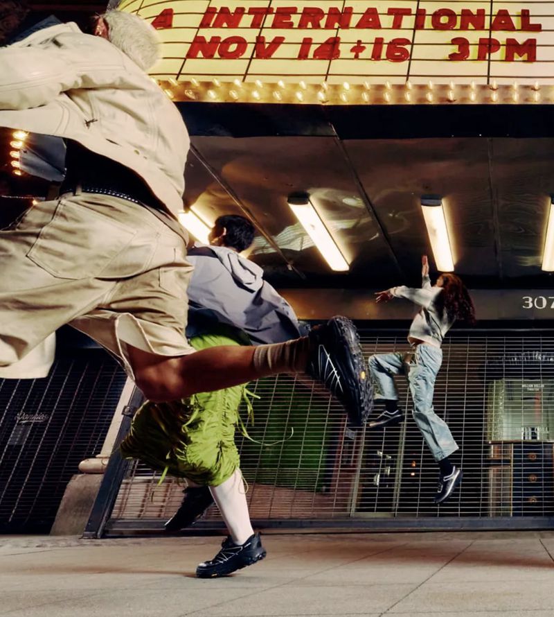 People running in an urban environment beneath an illuminated theater sign, captured with a low angle and a dynamic sense of motion.