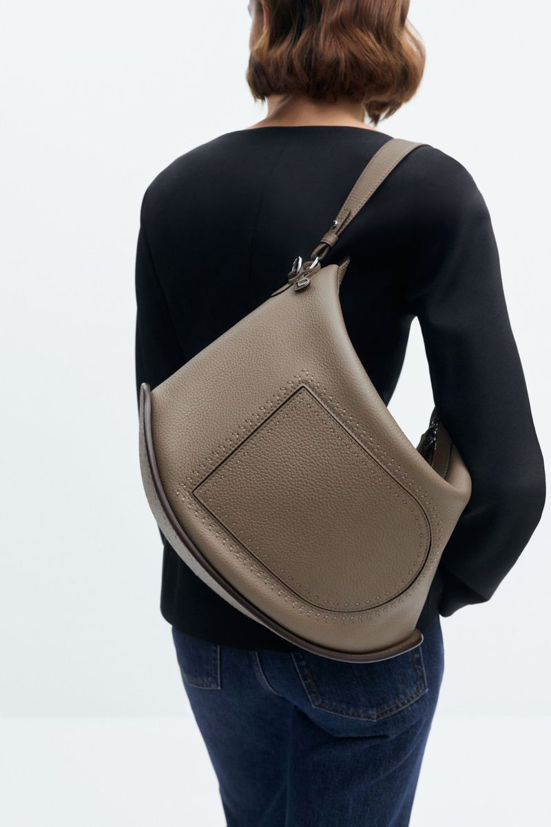 An adult female is seen from the back wearing a black long-sleeve shirt and jeans, carrying a large, crescent-shaped brown leather purse.
