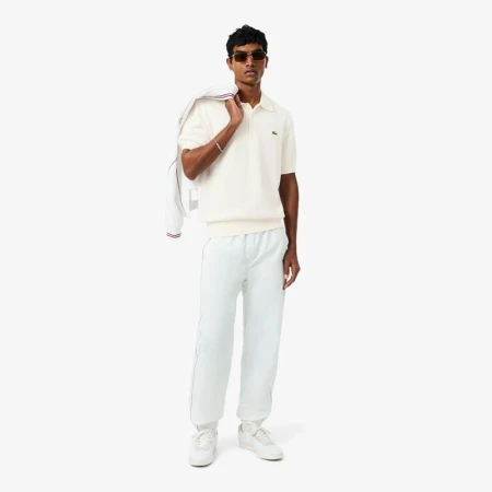 Full shot of an adult male in a polo shirt, sweatpants, and sunglasses holding a jacket against a white background. Fashion.