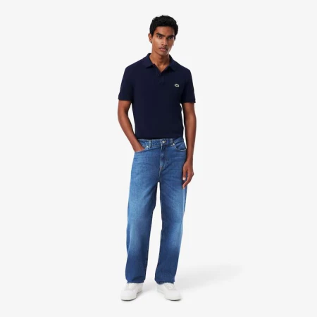 Full body shot of a slender adult male wearing a navy polo shirt, blue jeans, and white sneakers on a white background in a studio setting.