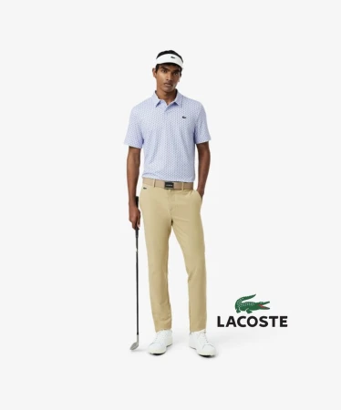 A male golf player in a blue and white patterned polo shirt and tan pants stands against a white background in a promotional shot.