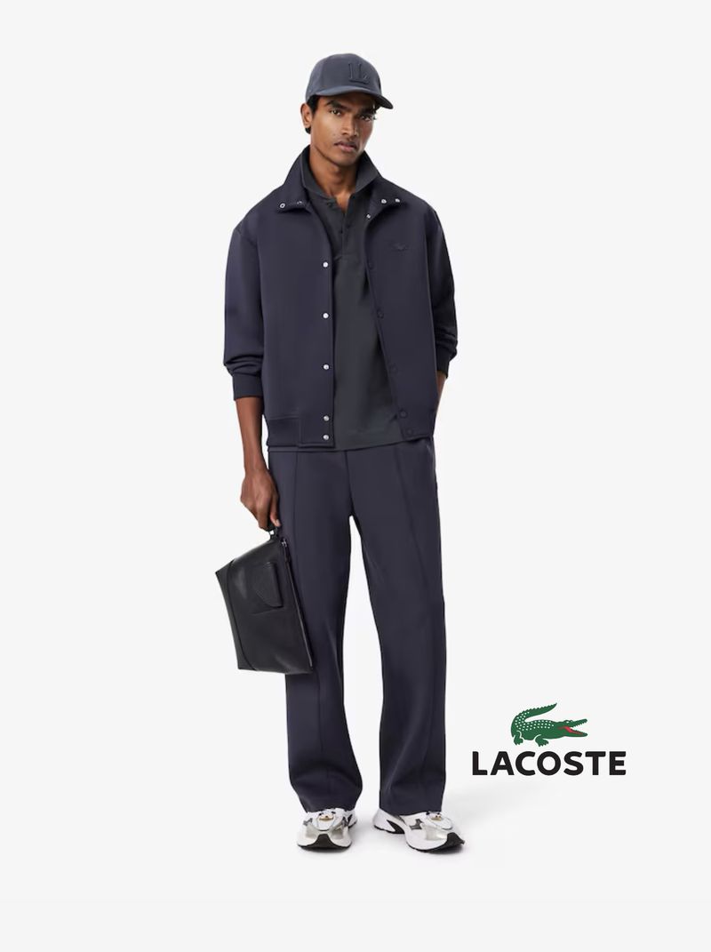 A full shot of a stylish adult male model in a matching dark blue jacket, pants, cap, and sneakers, posing against a clean white backdrop.