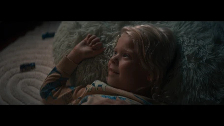 Young blond child lying on a textured light green rug with toy cars nearby for Queensland Hydro project.