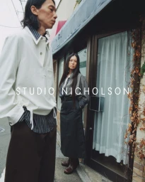 East Asian man in a white pullover and woman in a grey jacket standing outside a glass-door storefront for Studio Nicholson.