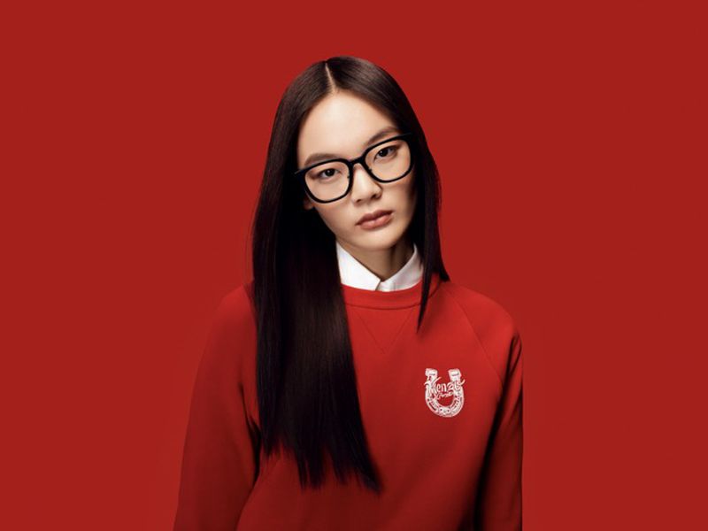 Portrait of a young Asian woman in a red sweater and glasses against a solid red backdrop, showcasing fashion and beauty.