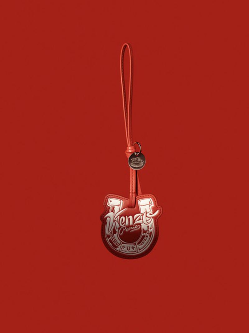 Kenzo horseshoe bag charm with a strap, set against a vibrant red background in a fashion-forward studio shot.