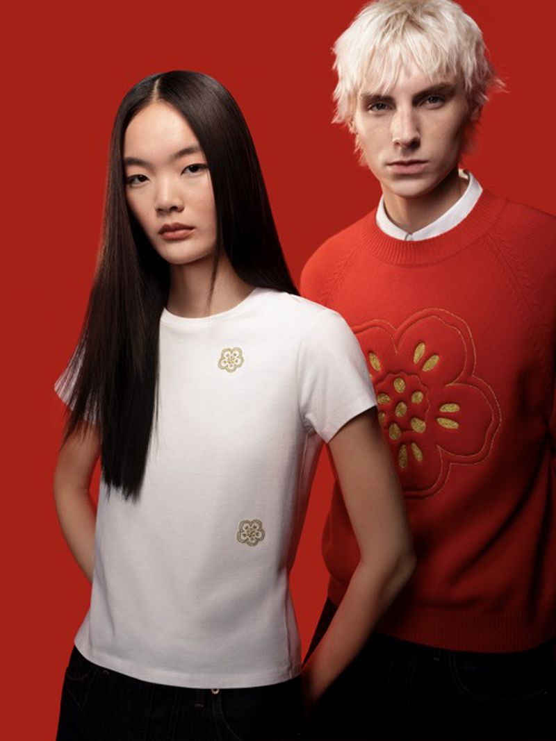 Two people in red and white floral-themed sweaters and t-shirts pose against a solid red background for a fashion editorial.
