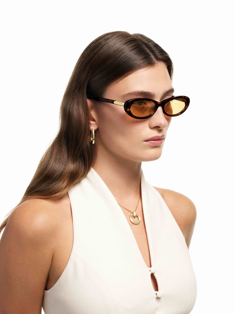 Portrait of a brunette woman wearing a white halter top and amber-tinted sunglasses against a stark white studio backdrop. Fashionable and chic.