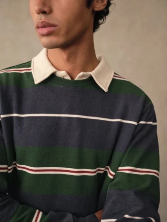 Close-up of a young adult man wearing a long-sleeved, horizontally striped rugby shirt in blue, green, and white against a neutral background.