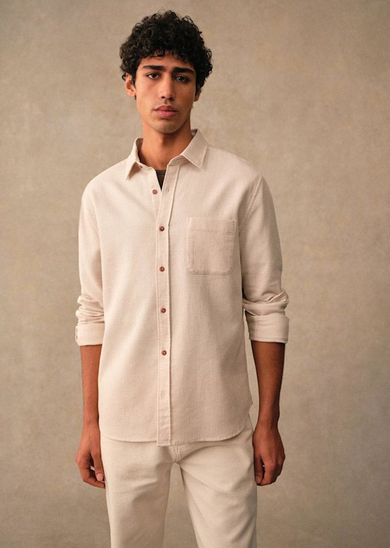 Maxime El Hanafi wearing a cream button-down shirt and matching trousers in a studio shoot for Octobre Editions.