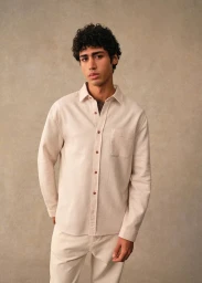 Model Maxime El Hanafi wearing a cream button-down overshirt and matching trousers against a neutral textured backdrop.