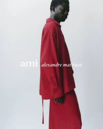 Profile view of a black man wearing a red shirt and red trousers against a plain white studio background