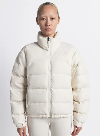 A person wears a cream-colored puffer jacket and matching pants in a studio shot, showcasing the garment's design and fit on a neutral backdrop.