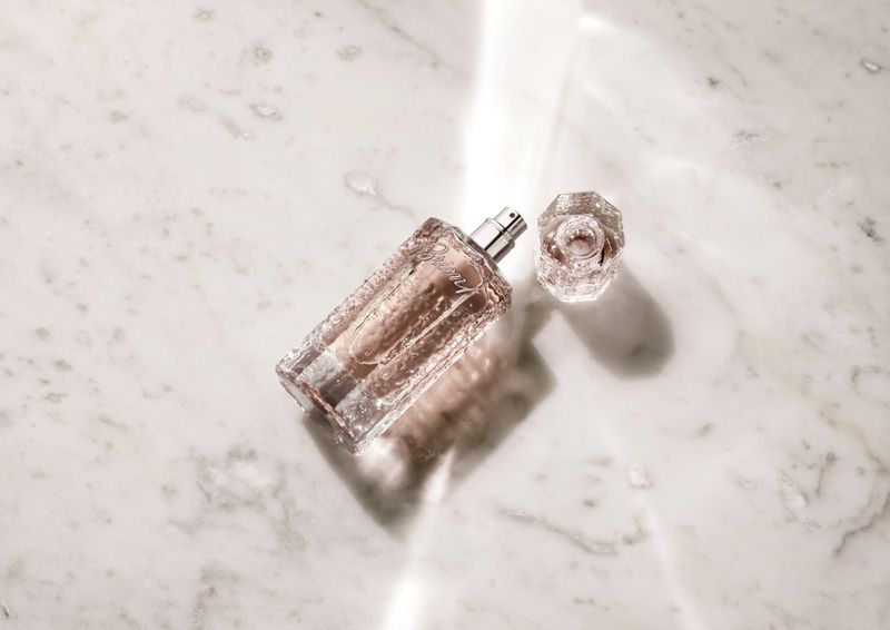 Elegant perfume bottle with crystal cap on a white marble surface, reflecting light. Beauty and fragrance concept.