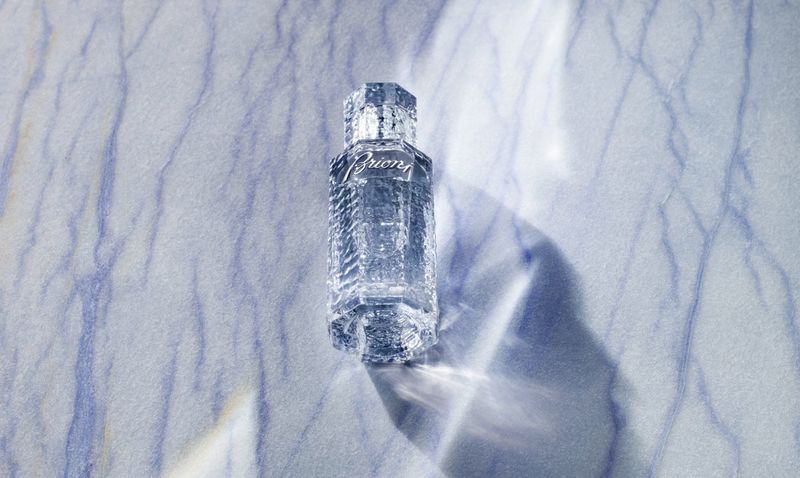 Crystal perfume bottle of Brioni fragrance against a blue and white marble background with subtle lighting and long shadows.