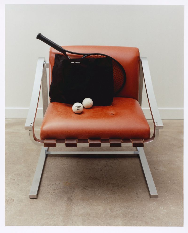 Stylish still life of tennis racket, tote bag, and balls arranged on a modern red chair against a neutral studio backdrop.