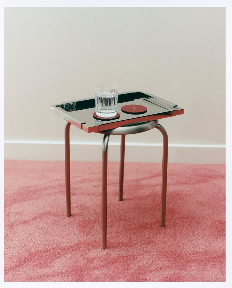 Still life shot of a glass of water and two coasters on a table with a pink carpet background.  Minimalist composition.