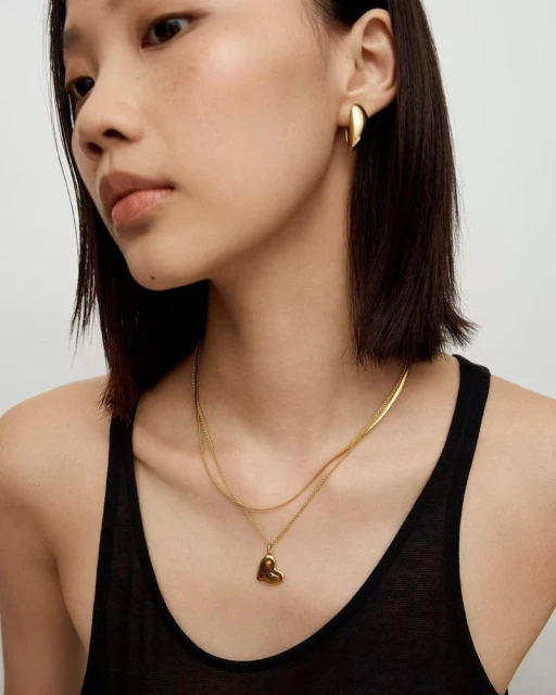 Woman wearing gold heart pendant necklace and gold earrings, close-up studio shot. Beauty and fashion product shot, gold jewelry.