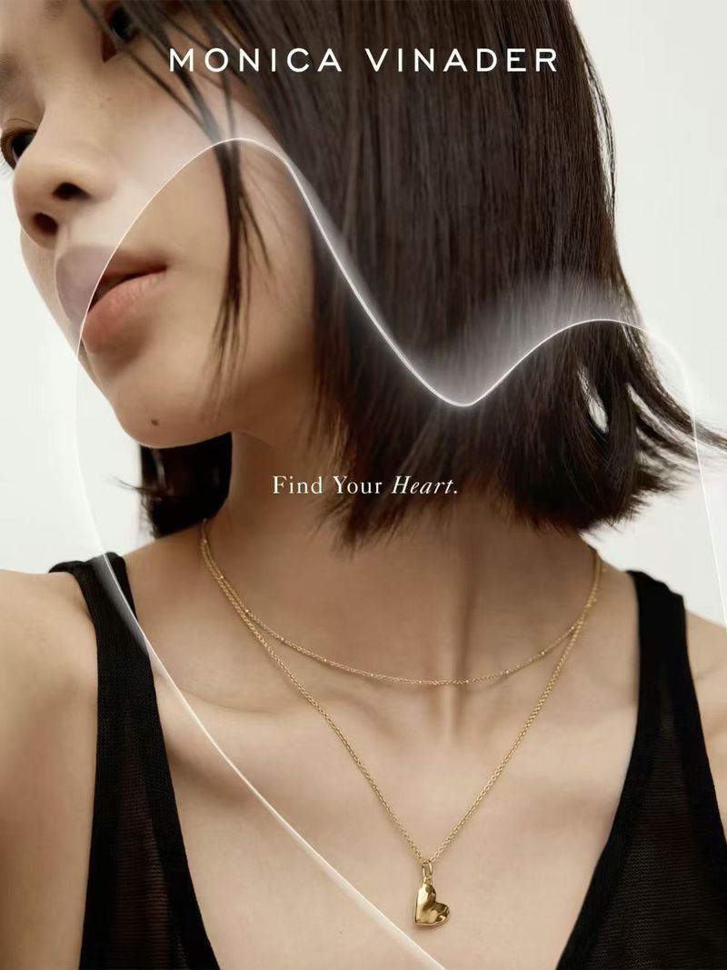 Young woman wearing a gold layered necklace with a heart pendant, against a white background in a close-up studio shot.