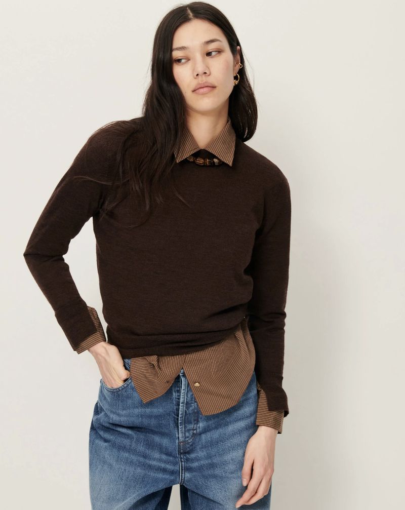 Portrait of a woman in a brown sweater and blue jeans against a white background, showcasing a casual fashion style.