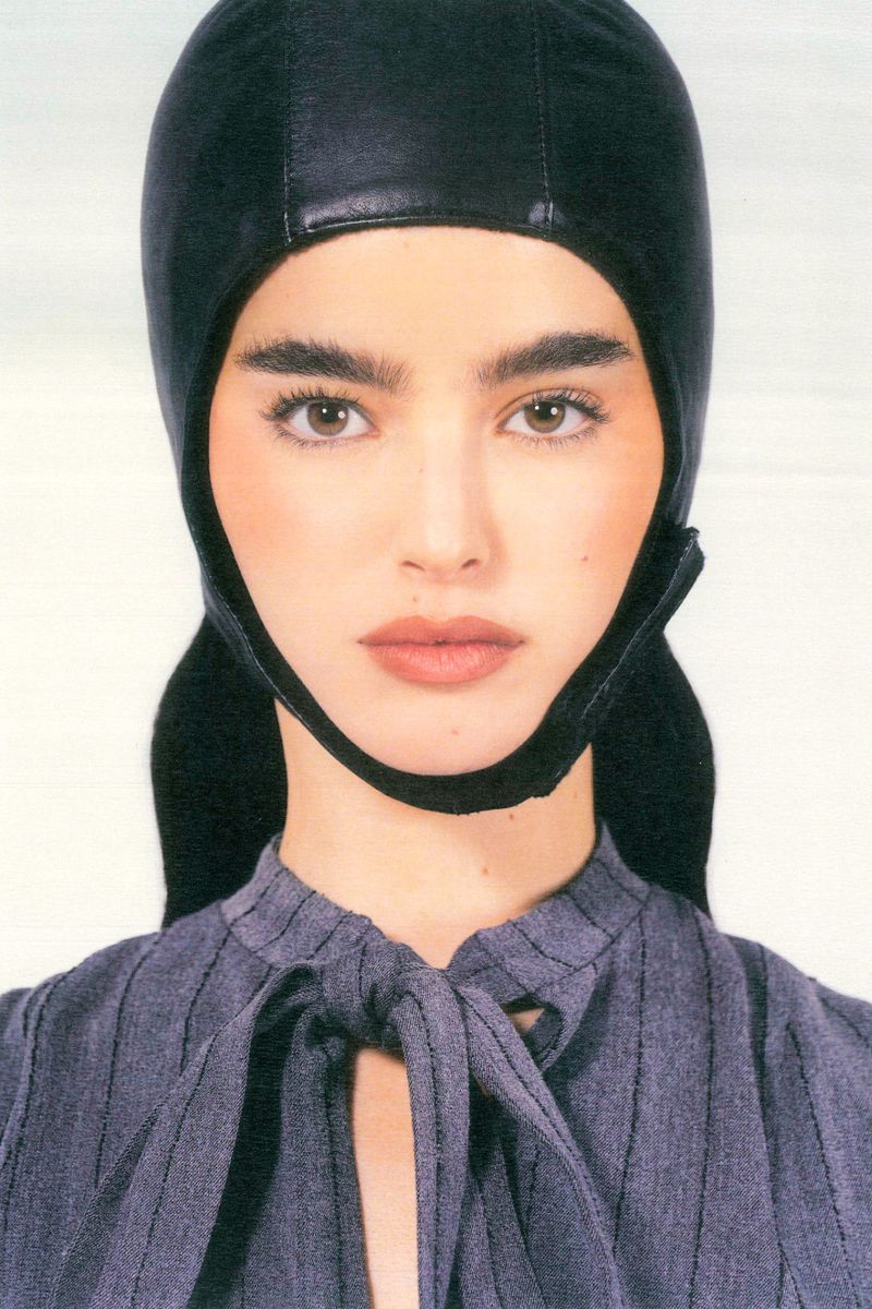 Close-up portrait of a woman with fair skin wearing a black head covering and a grey pinstripe blouse with a tied neckline.