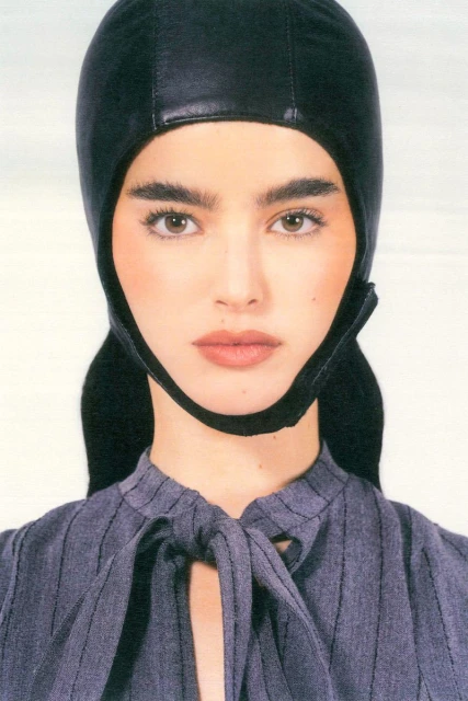 Close-up portrait of a woman with fair skin wearing a black head covering and a grey pinstripe blouse with a tied neckline.
