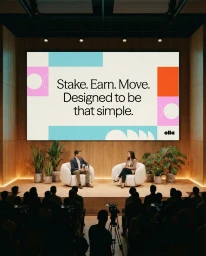 Two speakers seated on a wooden stage in white armchairs beneath a large screen presenting Olla brand identity to an audience.