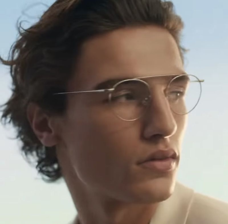 Close-up portrait of a man wearing round thin metal eyeglasses against a soft blue sky.