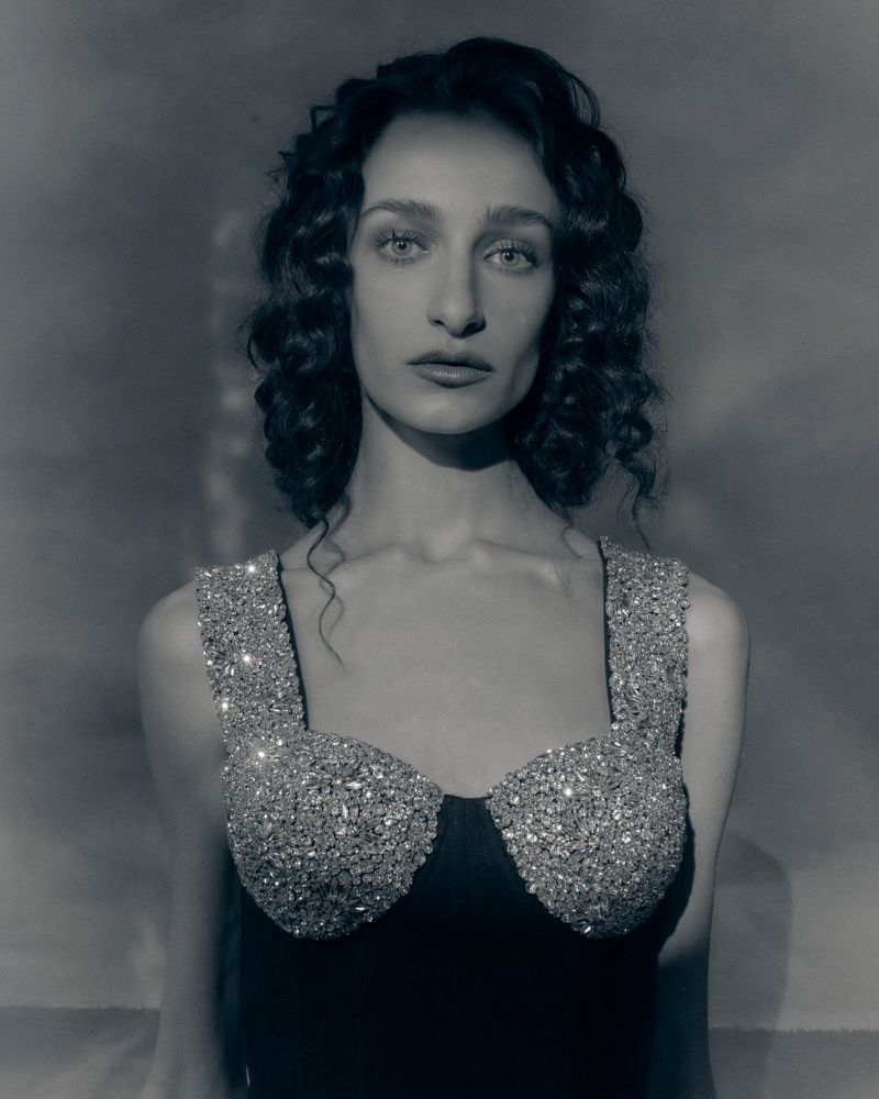 Portrait of a woman with dark curly hair wearing a heavily embellished crystal bodice against a mottled studio background