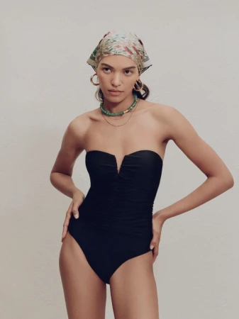 Woman in a black one-piece swimsuit, wearing a patterned headscarf, posing in a studio with a neutral background. Fashion shot.