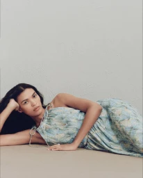 Model lying down wearing a blue patterned strapless dress against a neutral textured background.