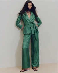 Model standing in a patterned green silk suit with a tied blazer against a pale studio background for Veronica Beard summer 2025.