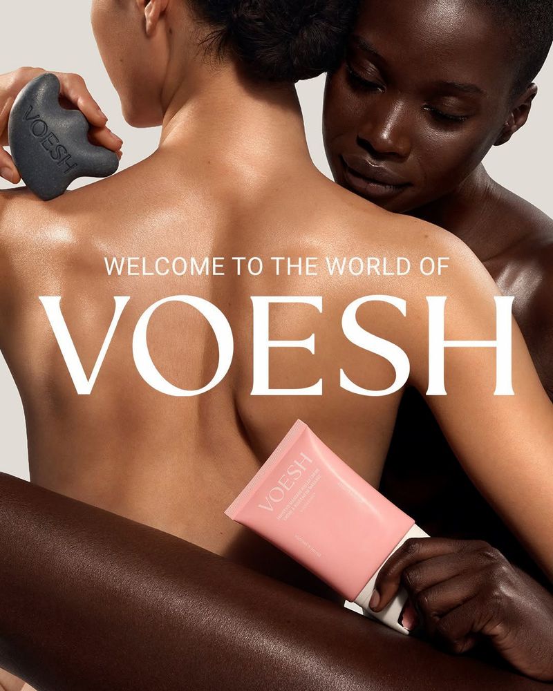 Two models showcasing glowing skin, holding a dark grey gua sha tool and a pink VOESH tube against a neutral backdrop.