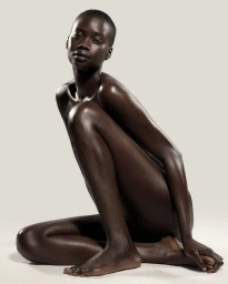 Model Fatou Jobe seated in a crouched pose with luminous glowing skin against an off-white seamless background.