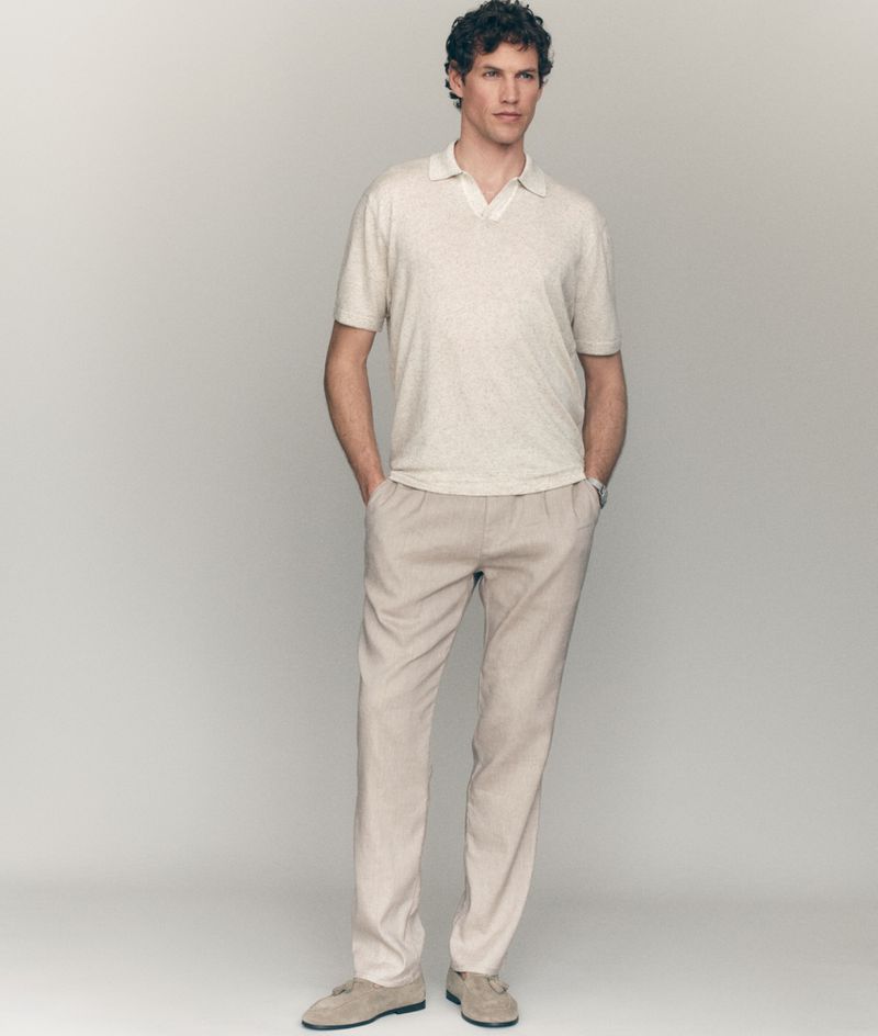 Model Paul Hupfer posing in a light cream polo shirt and relaxed beige trousers against a grey studio backdrop for Mavi Mens Summer 26.