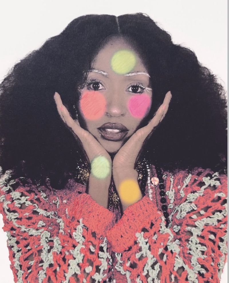 Ayo Edebiri posing with hands framing her face, styled with voluminous hair and colorful circle makeup against a white backdrop.
