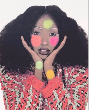 Ayo Edebiri posing with hands framing her face, styled with voluminous hair and colorful circle makeup against a white backdrop.