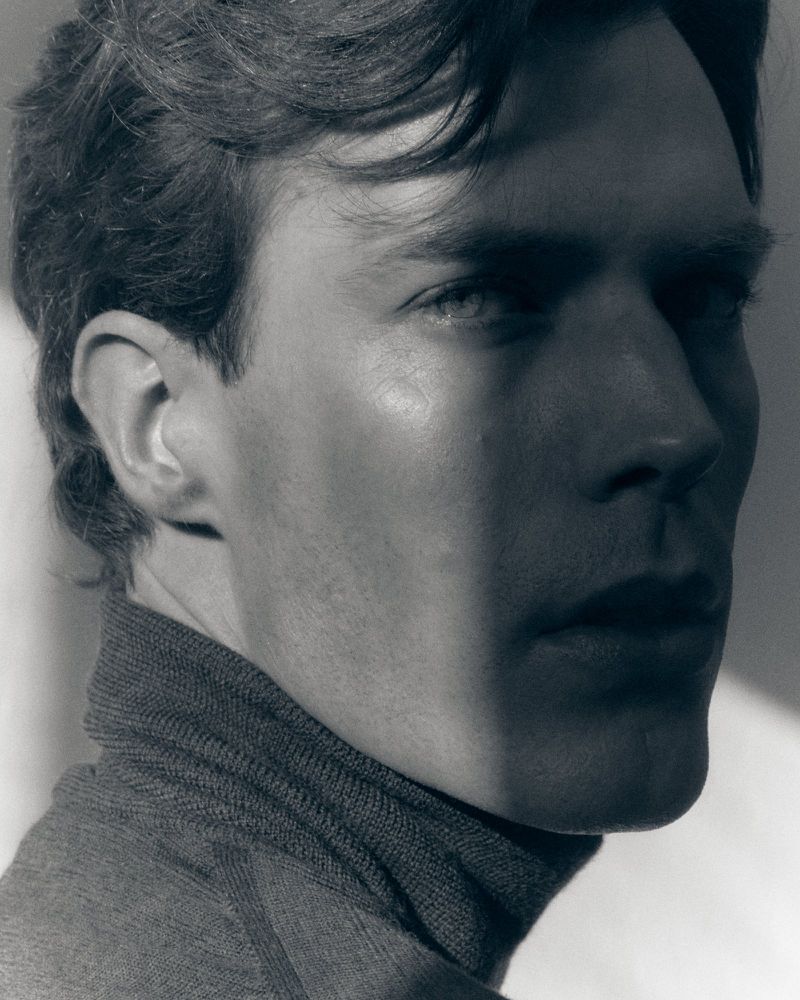Close-up monochrome portrait of a man in a dark turtleneck sweater looking towards the camera with dramatic side lighting