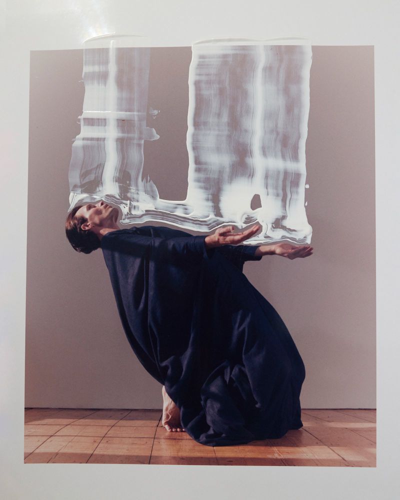Model kneeling in a dark navy robe with painted white brushstroke overlay across the top half of the portrait.