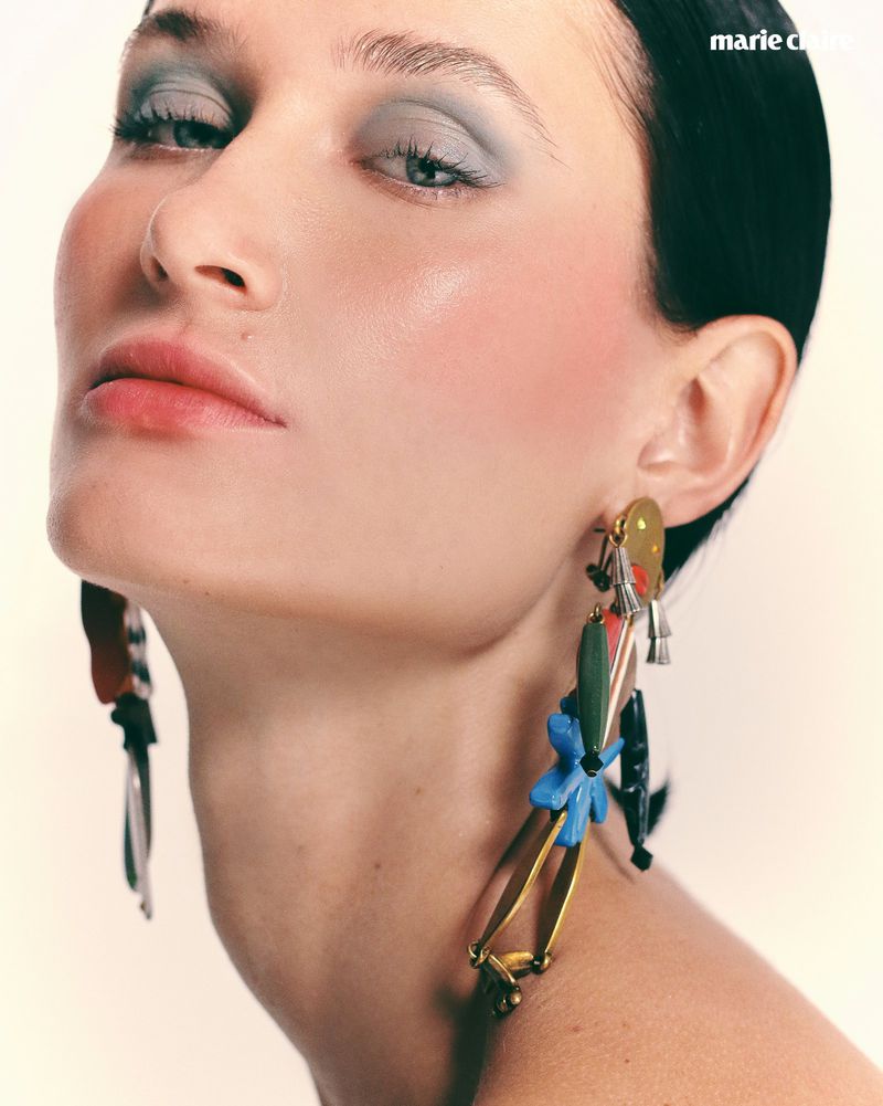 Beauty portrait of a woman with pastel blue eyeshadow and large dangling statement earrings against a pale backdrop.