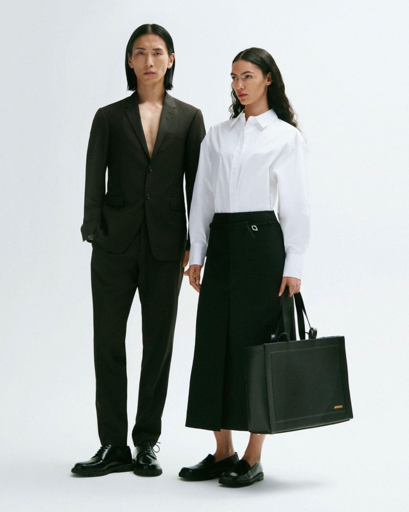 A stylish studio shot featuring an Asian male model in a suit and a female model in a white shirt and black skirt holding a tote bag.