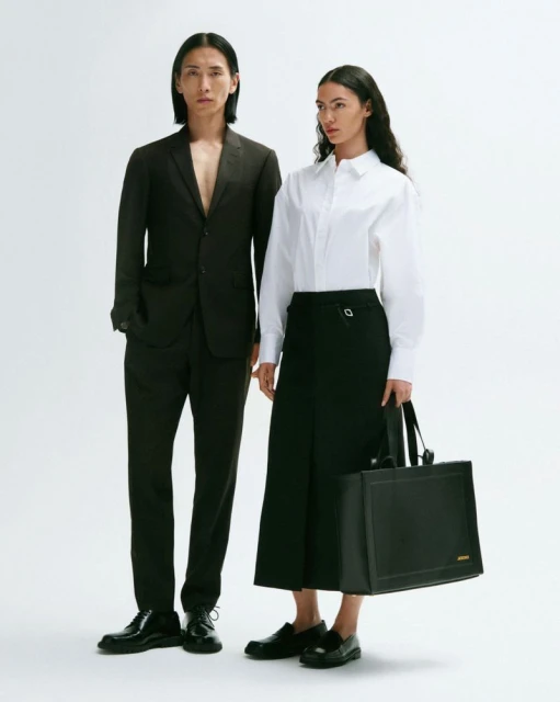 A stylish studio shot featuring an Asian male model in a suit and a female model in a white shirt and black skirt holding a tote bag.
