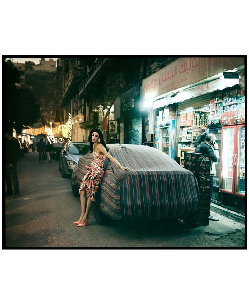 Model Nora Attal leaning against a covered car on an urban street at night outside a lighted shopfront.