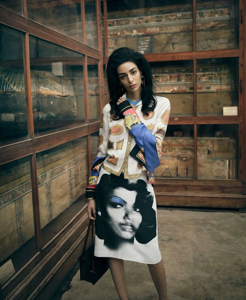 Model Nora Attal posing in a printed jacket and graphic face-print skirt inside a museum with tall wooden glass vitrines.