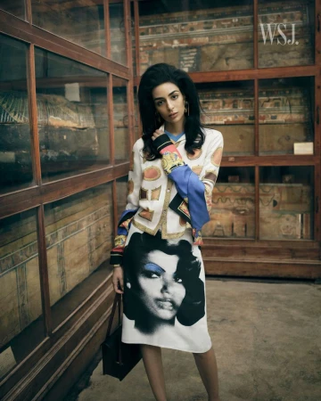 Model Nora Attal poses in a graphic print skirt suit in front of wooden museum display cases containing ancient artifacts.