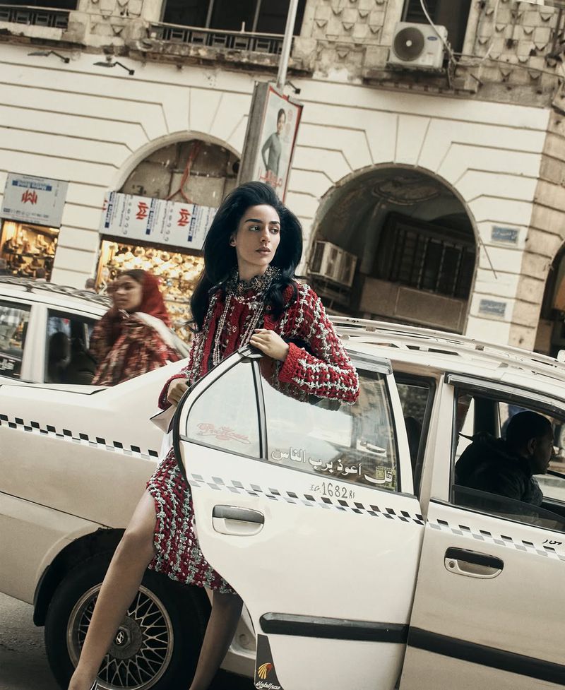 Model Nora Attal wearing a red patterned tweed dress stepping out of a white taxi on a downtown Cairo city street.