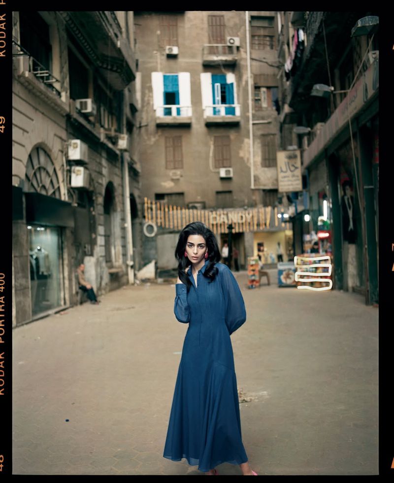 Model Nora Attal posing in a flowing teal blue long-sleeved dress in the center of a downtown Cairo street.