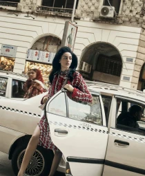 Model Nora Attal wearing a red patterned tweed dress stepping out of a white taxi on a downtown Cairo city street.