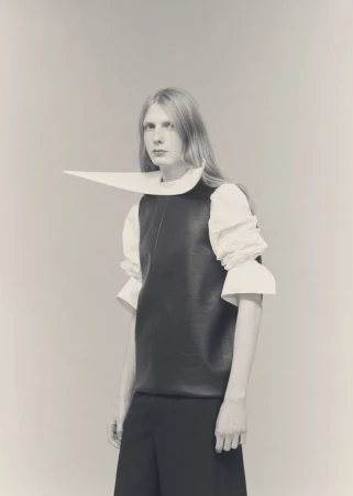 Model Filip Bryndza wearing an avant-garde pointed white collar top and dark vest against a neutral studio backdrop.