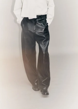 Cropped view of a model wearing wide-leg black leather trousers and a loose white shirt against a neutral studio backdrop.